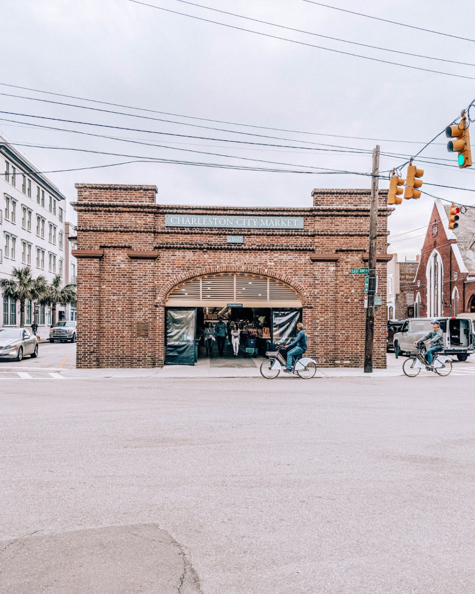 Building that says "Charleston City Market" with bicycles riding in front on the road