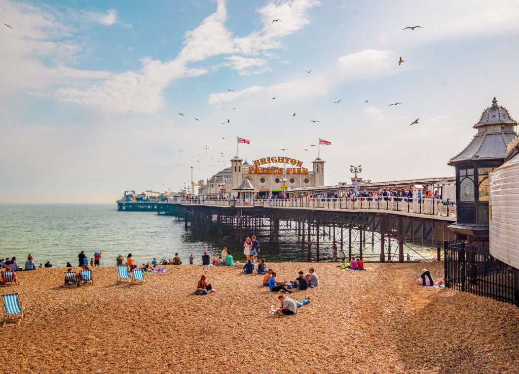 Bustling Brighton Pier with people sitting on beach chairs on the shore below